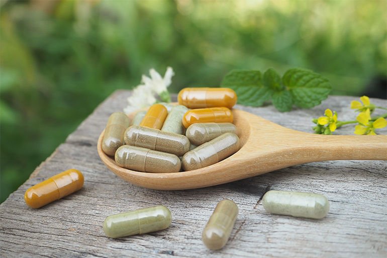 Wooden spoon on a rustic surface with assorted herbal capsules